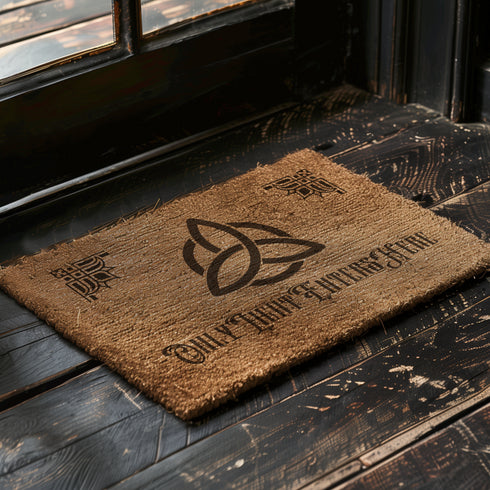 Coir doormat featuring large triple moon and triquetra symbol in center, surrounded by celestial designs including stars and moon phases, all in dark brown on natural tan background.